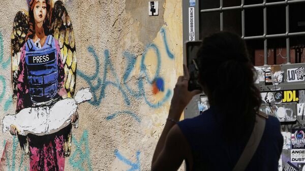 Uma mulher tira uma foto da imagem O anjo, pintada no início deste ano pelo artista de rua Harry Greb, dedicada aos jornalistas mortos em Gaza - Sputnik Brasil