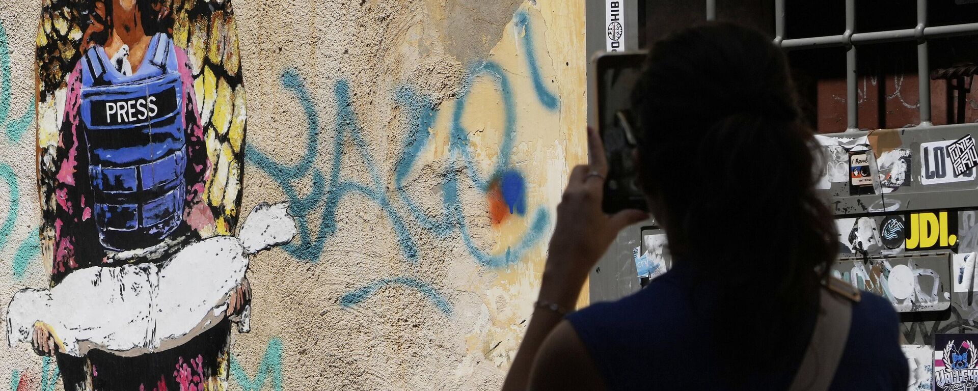 Uma mulher tira uma foto da imagem O anjo, pintada no início deste ano pelo artista de rua Harry Greb, dedicada aos jornalistas mortos em Gaza - Sputnik Brasil, 1920, 25.08.2025