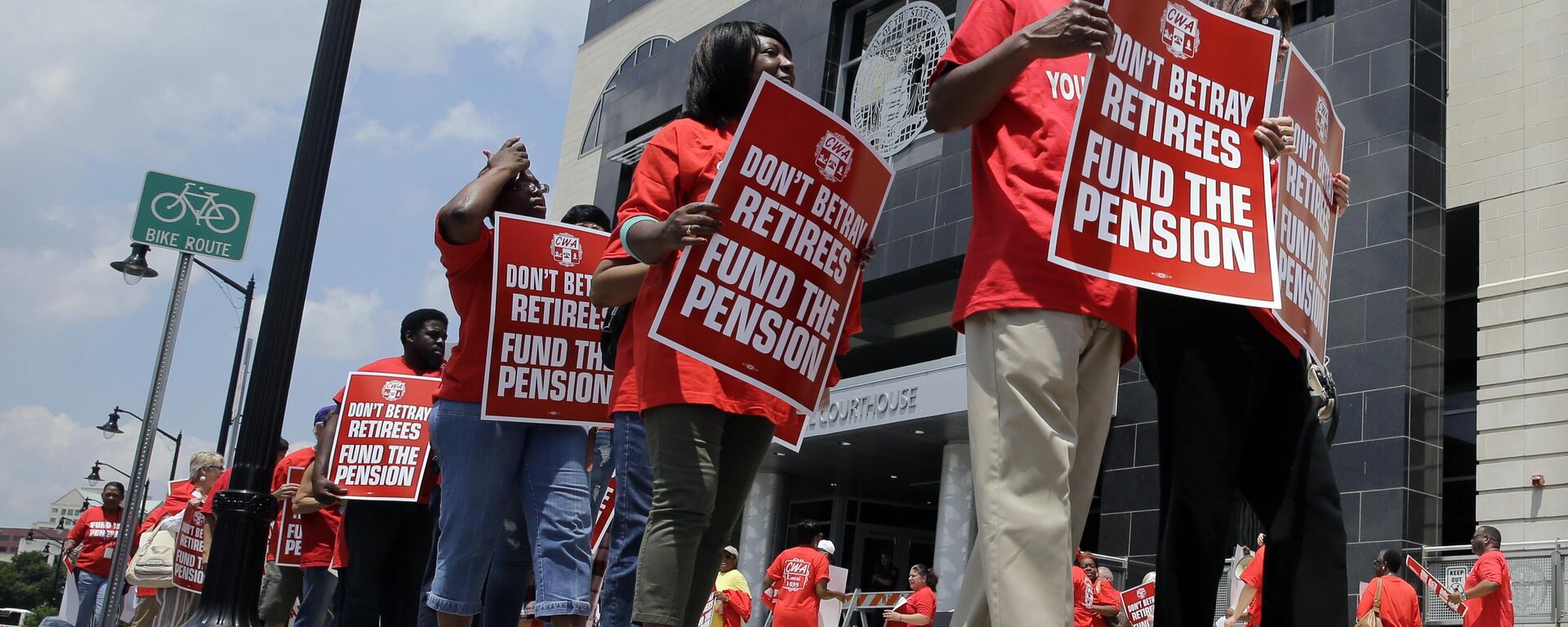 Manifestantes carregam cartazes de protesto enquanto marcham contra a decisão de usar o pagamento de pensões para equilibrar o orçamento em Trenton, Nova Jersey. EUA, 25 de junho de 2014 - Sputnik Brasil, 1920, 28.08.2025