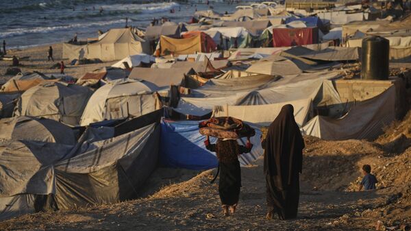 Palestinos deslocados caminham por um acampamento improvisado ao longo da costa de Deir al-Balah, na Faixa de Gaza, em setembro de 2025 - Sputnik Brasil