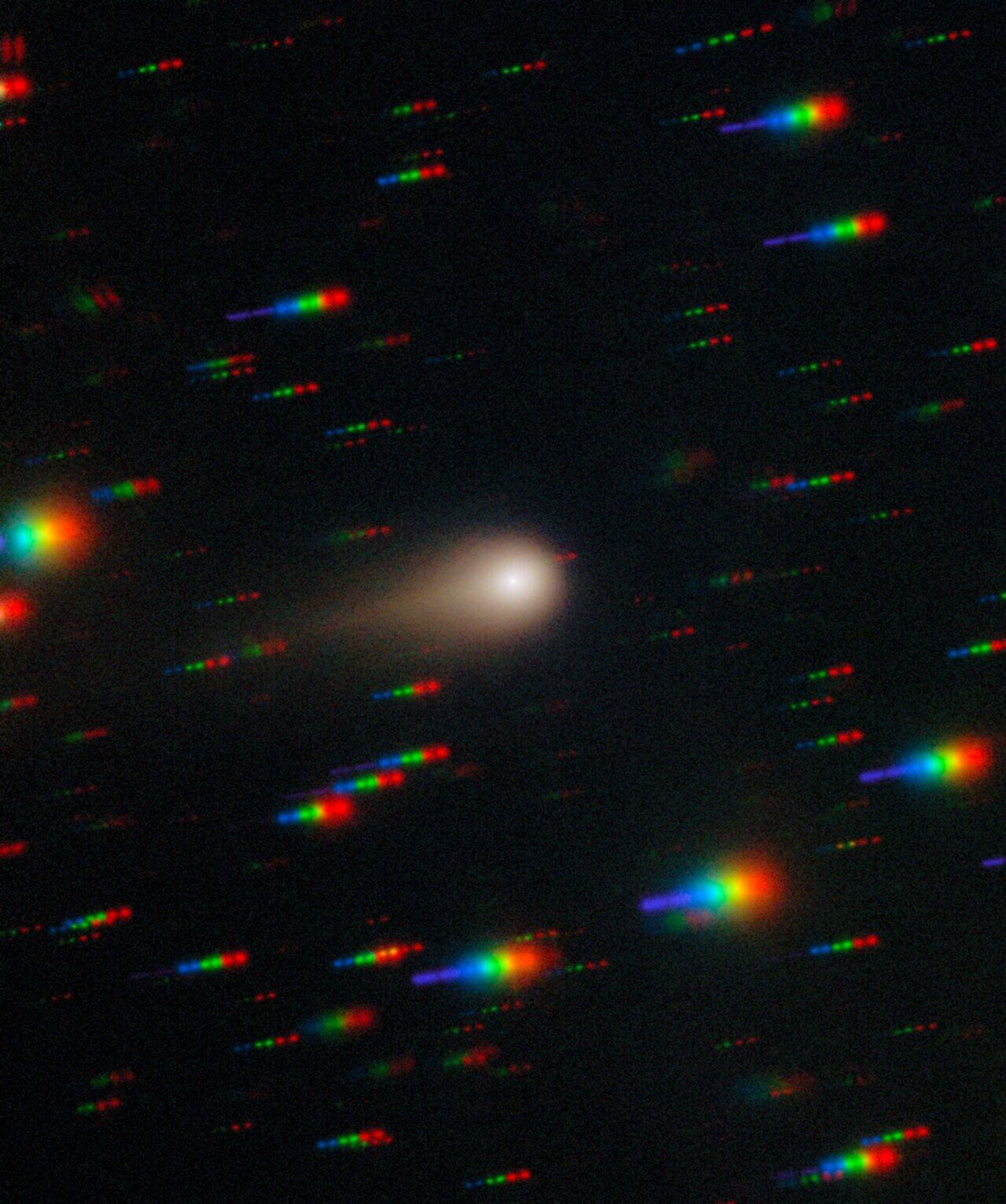 O cometa 3I/ATLAS atravessa um denso campo estelar nesta imagem capturada pelo Gemini Multi-Object Spectrograph (GMOS) no Gemini Sul, em Cerro Pachón, no Chile. A imagem é composta por exposições obtidas por meio de quatro filtros — vermelho, verde, azul e ultravioleta. À medida que as exposições são obtidas, o cometa permanece fixo no centro do campo de visão do telescópio. No entanto, as posições das estrelas de fundo mudam em relação ao cometa, fazendo com que apareçam como listras coloridas na imagem final O cometa 3I/ATLAS atravessa um denso campo estelar nesta imagem capturada pelo Gemini Multi-Object Spectrograph (GMOS) no Gemini Sul, em Cerro Pachón, no Chile. A imagem é composta por exposições obtidas por meio de quatro filtros — vermelho, verde, azul e ultravioleta. À medida que as exposições são obtidas, o cometa permanece fixo no centro do campo de visão do telescópio. No entanto, as posições das estrelas de fundo mudam em relação ao cometa, fazendo com que apareçam como listras coloridas na imagem final