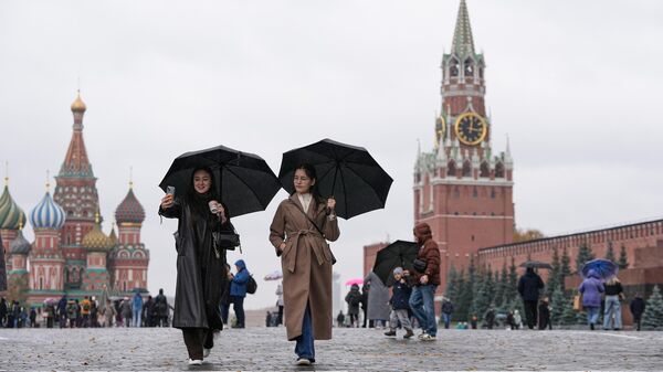 Pessoas caminham sob a chuva pela Praça Vermelha, com a Catedral de São Basílio à esquerda e a Torre Spasskaya ao fundo, em Moscou. Rússia, 17 de outubro de 2025 - Sputnik Brasil