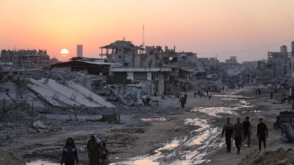 Palestinos caminham entre prédios destruídos em Khan Younis, no sul da Faixa de Gaza, em novembro de 2025 - Sputnik Brasil