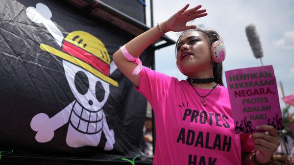 Ativista segura cartaz e ao fundo uma bandeira do personagem One Piece. - Sputnik Brasil