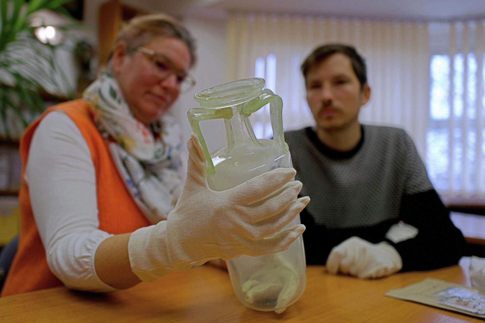 Arqueólogos húngaros observando vaso de vidro encontrado no sarcófago