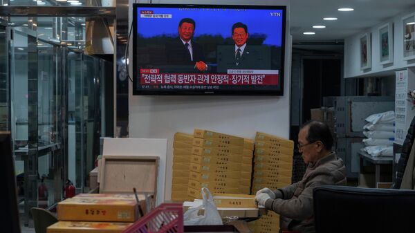 Um homem empacotando produtos em uma padaria enquanto uma televisão mostra o presidente chinês Xi Jinping (E) e o presidente sul-coreano Lee Jae Myung apertando as mãos durante uma reunião bilateral à margem da Cúpula da Cooperação Econômica Ásia-Pacífico (APEC) de 2025, realizada em Gyeongju, Coreia do Sul, 1º de novembro de 2025 - Sputnik Brasil