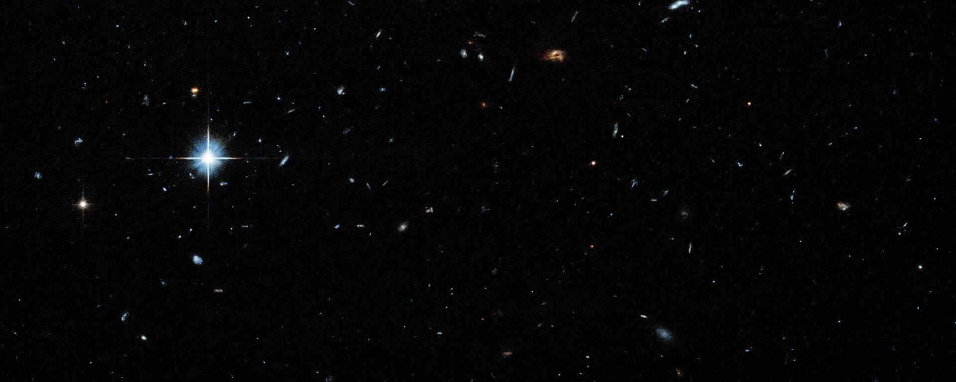 Um campo escuro com estrelas e galáxias de vários tamanhos espalhadas por toda a imagem. Uma estrela particularmente brilhante é visível na região superior esquerda - Sputnik Brasil, 1920, 07.01.2026
