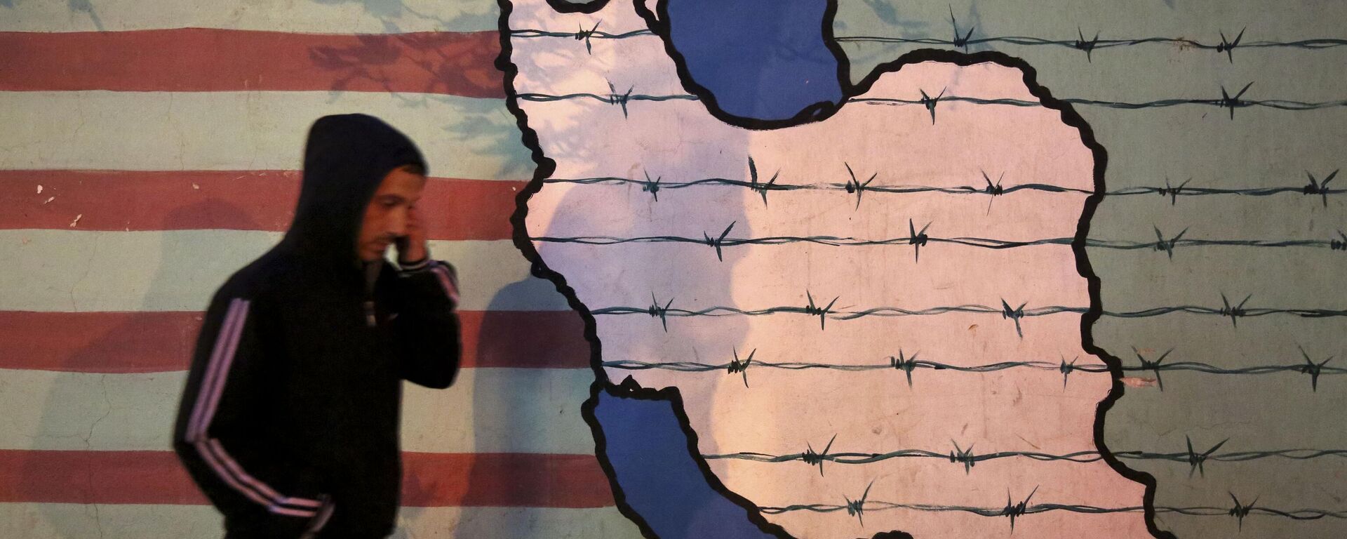 Um homem caminha ao lado de um mural anti-EUA, pintado na parede da antiga embaixada norte-americana, em Teerã, Irã, 2 de novembro de 2013 - Sputnik Brasil, 1920, 28.01.2026