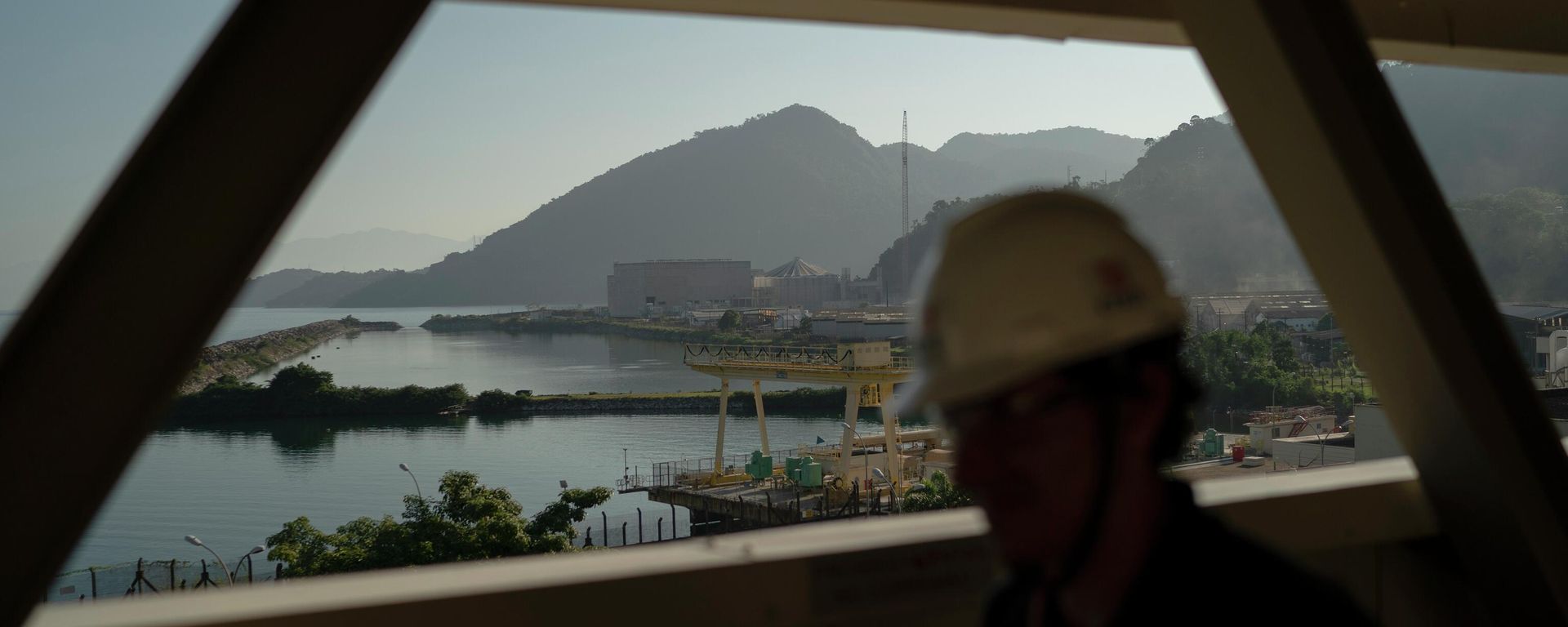 Um funcionário caminha sobre uma passarela de acesso, tendo como pano de fundo o reator nuclear Angra 3, no complexo da Usina Nuclear de Angra. Angra dos Reis, Rio de Janeiro - Sputnik Brasil, 1920, 16.03.2026