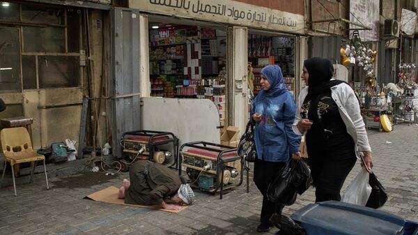 Mulheres passam por um homem que reza na calçada no centro de Bagdá, Iraque, 25 de março de 2026 - Sputnik Brasil