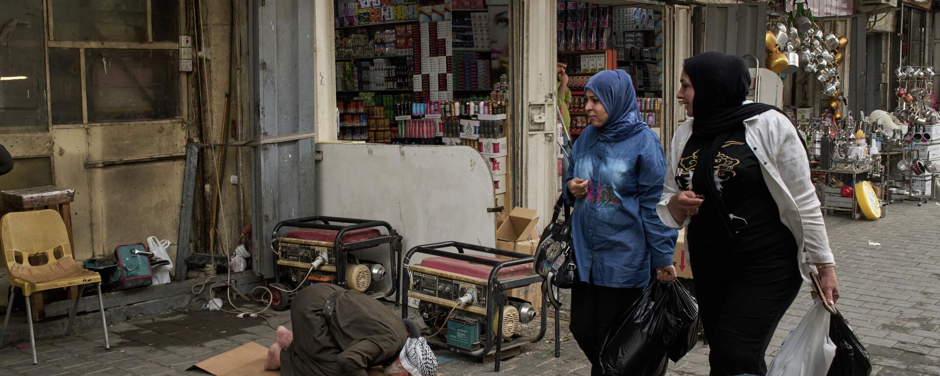 Mulheres passam por um homem que reza na calçada no centro de Bagdá, Iraque, 25 de março de 2026 - Sputnik Brasil, 1920, 26.03.2026