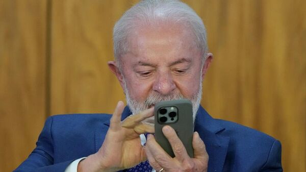 O presidente do Brasil, Luiz Inácio Lula da Silva, observa o celular de um assessor durante a cerimônia de assinatura do Plano Brasil Soberano, no Palácio do Planalto, em Brasília, 13 de agosto de 2025 - Sputnik Brasil