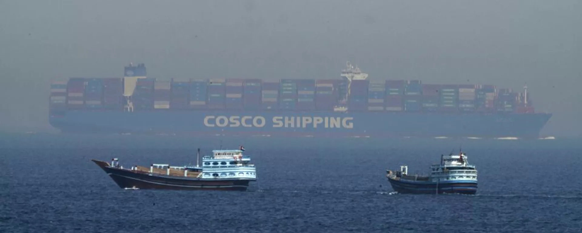 Dois dhows tradicionais navegam ao lado de um grande navio porta-contentores no estreito de Ormuz, 19 de maio de 2023 - Sputnik Brasil, 1920, 18.04.2026