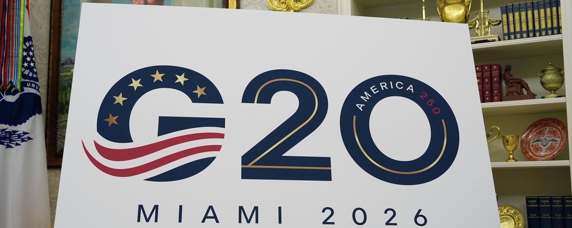 Uma placa anunciando a realização da cúpula do G20 em Miami em 2026 é exibida enquanto Donald Trump discursa no Salão Oval da Casa Branca, em Washington DC. EUA, 5 de setembro de 2025  - Sputnik Brasil, 1920, 26.04.2026