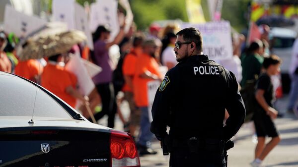Um policial de Uvalde observa familiares e amigos das vítimas fatais e feridas no tiroteio na Escola Primária Robb participarem de uma marcha e manifestação de protesto em Uvalde, Texas, 10 de julho de 2022 - Sputnik Brasil