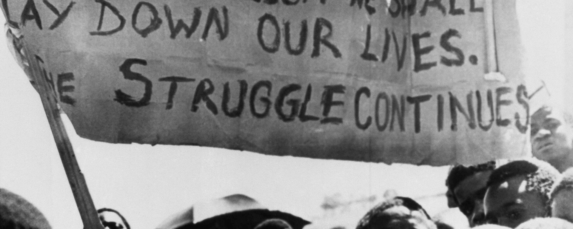 Uma faixa é erguida acima de estudantes negros em Joanesburgo, no bairro de Soweto, onde se reuniram após o funeral de um estudante negro de 16 anos que morreu na prisão. África do Sul, 18 de outubro de 1976 - Sputnik Brasil, 1920, 19.06.2026