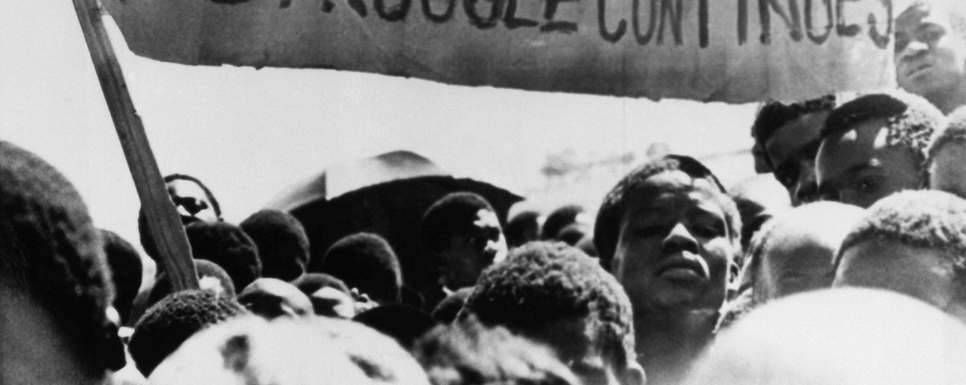 Uma faixa é erguida acima de estudantes negros em Joanesburgo, no bairro de Soweto, onde se reuniram após o funeral de um estudante negro de 16 anos que morreu na prisão. África do Sul, 18 de outubro de 1976 - Sputnik Brasil, 1920, 19.06.2026