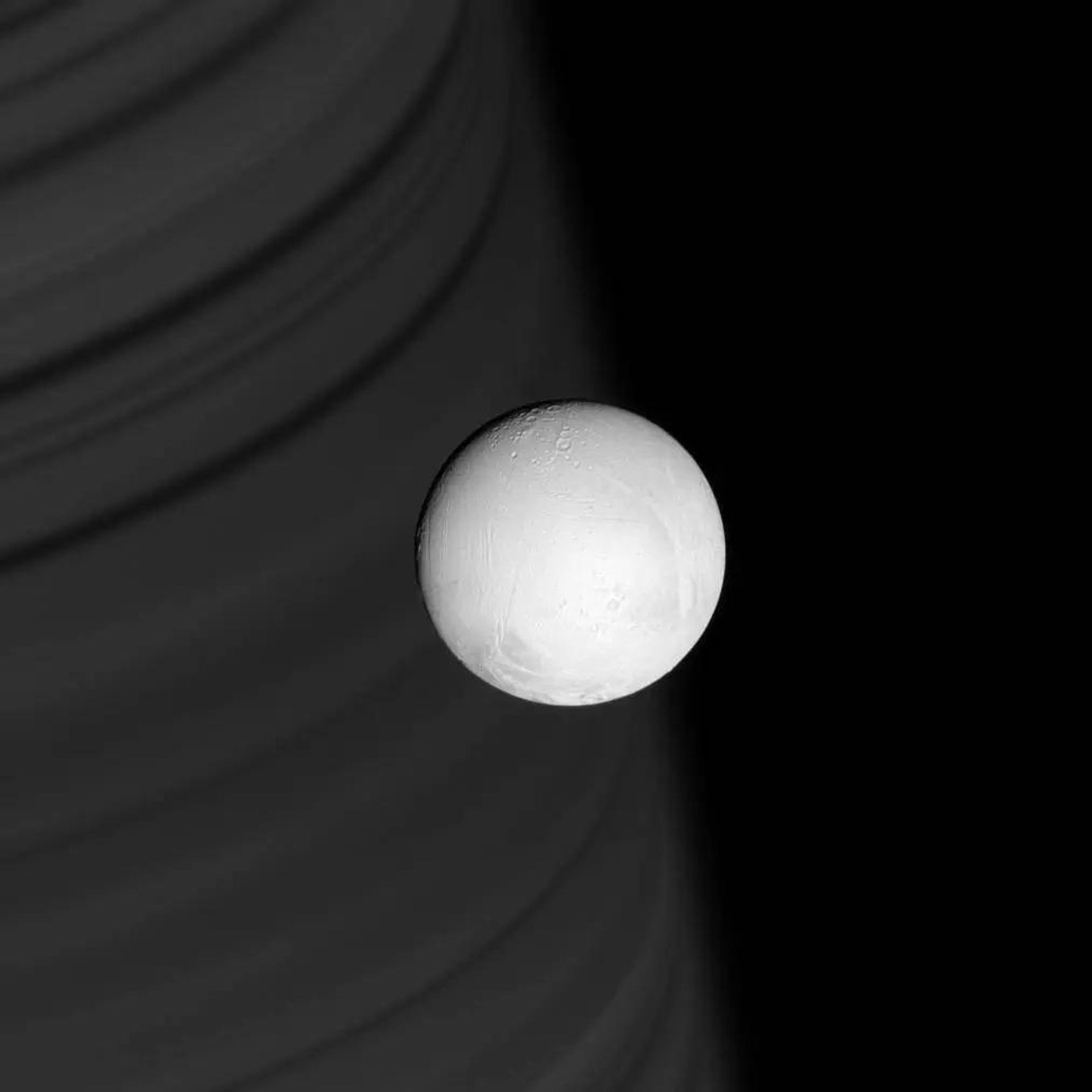 As sombras dos anéis delineiam a face do distante Saturno, servindo de pano de fundo para a brilhante esfera branca de Encélado. Esta lua gelada, com sua superfície bastante modificada e imponente pluma de material gelado, é alvo de intenso estudo da Cassini durante sua missão Equinox As sombras dos anéis delineiam a face do distante Saturno, servindo de pano de fundo para a brilhante esfera branca de Encélado. Esta lua gelada, com sua superfície bastante modificada e imponente pluma de material gelado, é alvo de intenso estudo da Cassini durante sua missão Equinox