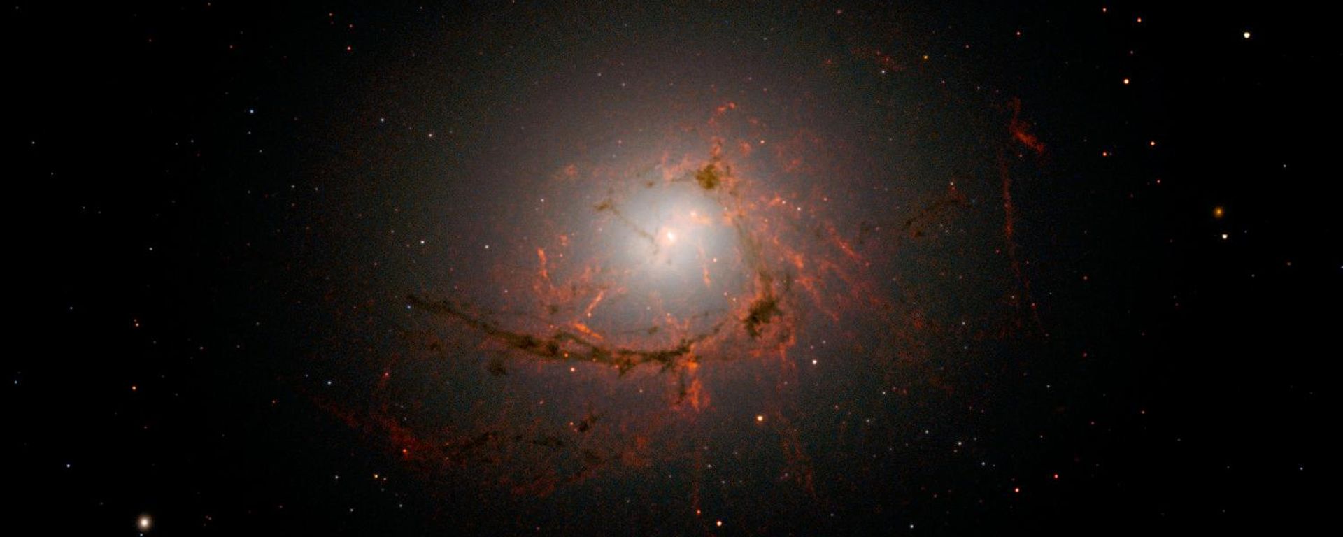 Esta imagem, captada pela Wide Field Camera 3 (WFC3) do Hubble, mostra NGC 4696, a maior galáxia do Aglomerado de Centauro. As novas imagens revelam, com detalhes inéditos, os filamentos de poeira que envolvem o centro dessa enorme galáxia. Esses filamentos se curvam e espiralam para dentro em uma forma intrigante, girando ao redor do buraco negro supermassivo a tal distância que acabam sendo arrastados e, eventualmente, consumidos por ele - Sputnik Brasil, 1920, 20.07.2026