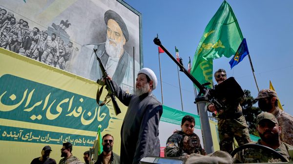 Um clérigo xiita armado passa, a bordo de um veículo militar, por um painel que retrata o aiatolá Ruhollah Khomeini, fundador da República Islâmica do Irã, durante o desfile de estilo militar Janfada — ou Sacrifício pelo Irã —, organizado pelo Estado em Teerã, Irã, em 18 de setembro de 2026 - Sputnik Brasil