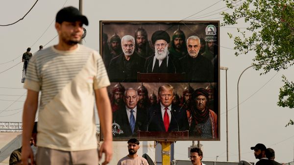 Homem passa por um painel com as imagens do comandante de milícia iraquiano morto Abu Mahdi al-Muhandis (no alto, à esquerda), do falecido líder supremo do Irã, aiatolá Ali Khamenei (no alto, ao centro), e do comandante iraniano morto Qassem Soleimani (no alto, à direita) — posicionadas acima dos retratos do primeiro-ministro de Israel, Benjamin Netanyahu (na parte inferior, à esquerda), e do presidente dos EUA, Donald Trump (na parte inferior, ao centro) — durante as celebrações que marcaram a retirada completa das tropas dos EUA do Iraque. Bagdá, Iraque, 30 de setembro de 2026 - Sputnik Brasil