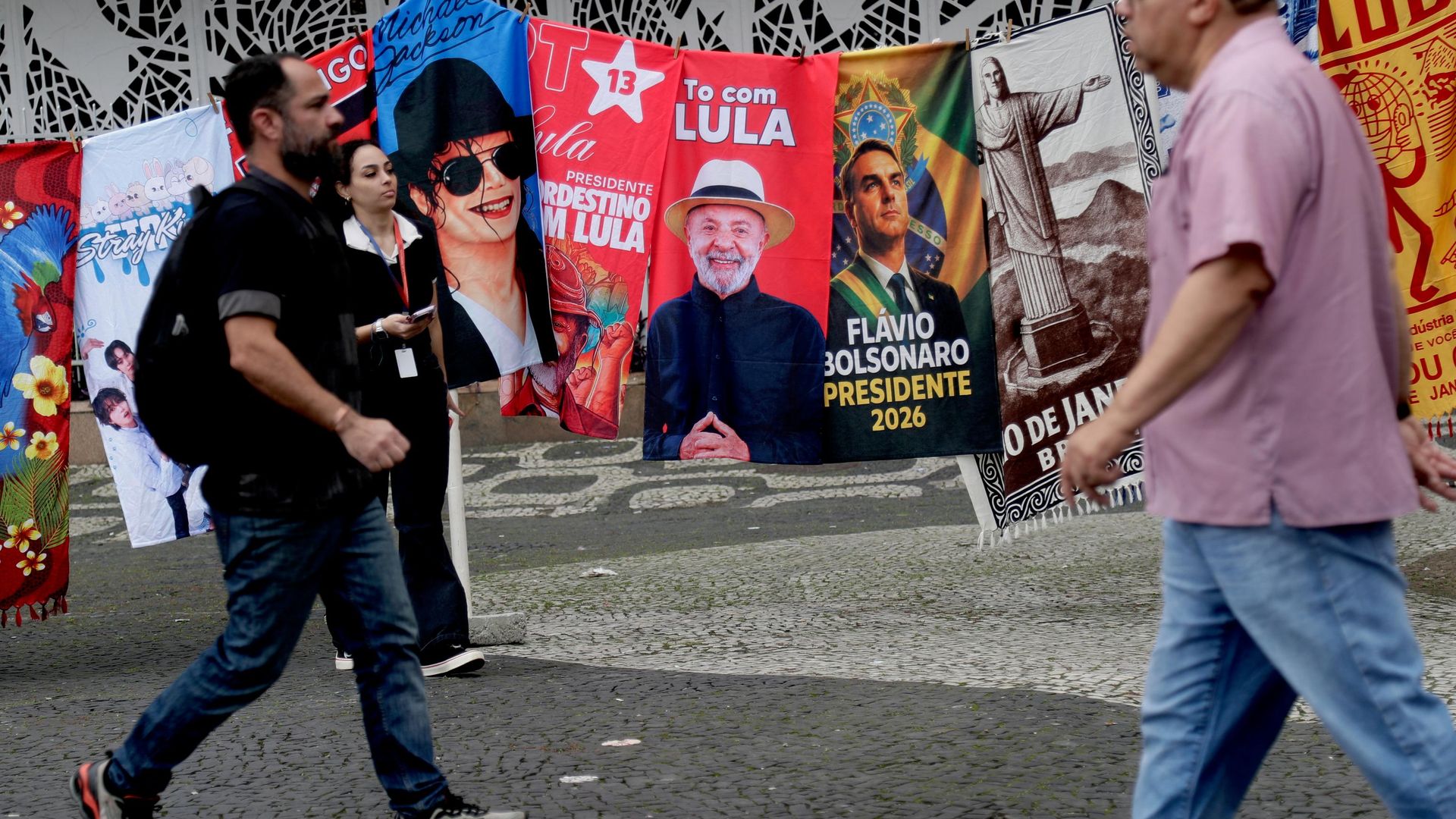 Pessoas passam por bandeiras de campanha do presidente brasileiro Luiz Inácio Lula da Silva, que concorre à reeleição, e do candidato presidencial da oposição, senador Flávio Bolsonaro, no dia seguinte às eleições gerais no Rio de Janeiro, 5 de outubro de 2026 - Sputnik Brasil, 1920, 10.10.2026