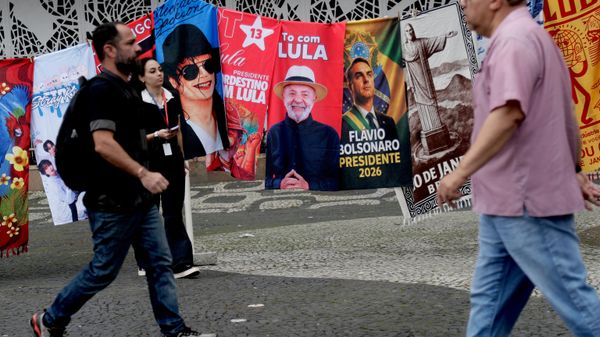 Pessoas passam por bandeiras de campanha do presidente brasileiro Luiz Inácio Lula da Silva, que concorre à reeleição, e do candidato presidencial da oposição, senador Flávio Bolsonaro, no dia seguinte às eleições gerais no Rio de Janeiro, 5 de outubro de 2026 - Sputnik Brasil