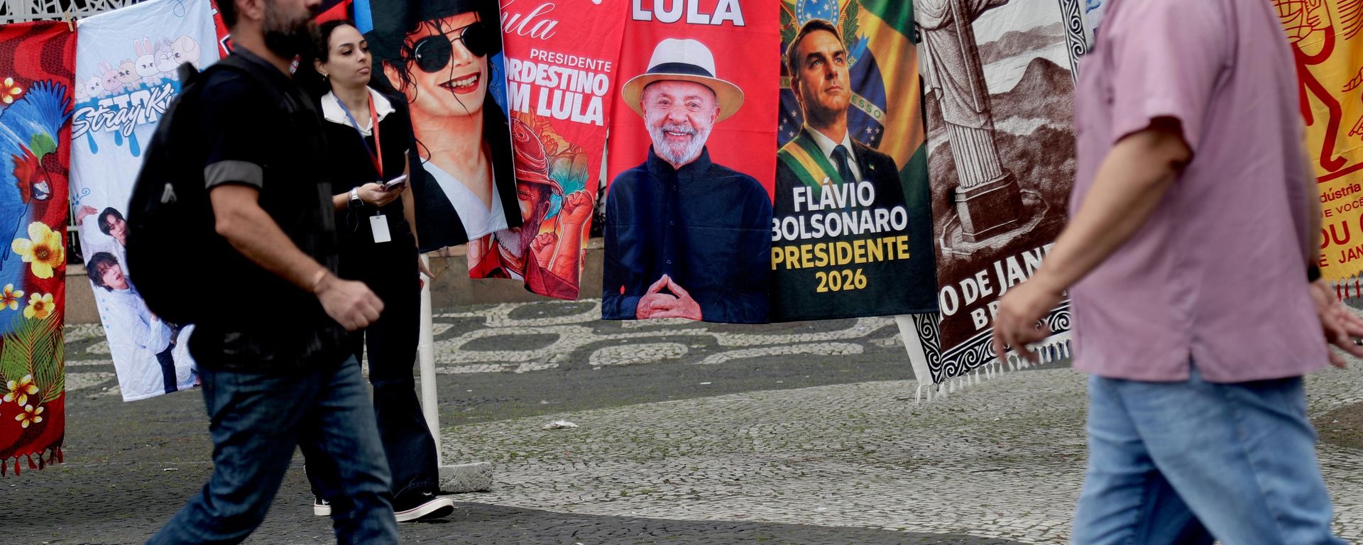 Pessoas passam por bandeiras de campanha do presidente brasileiro Luiz Inácio Lula da Silva, que concorre à reeleição, e do candidato presidencial da oposição, senador Flávio Bolsonaro, no dia seguinte às eleições gerais no Rio de Janeiro, 5 de outubro de 2026 - Sputnik Brasil, 1920, 10.10.2026