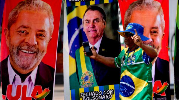 Um manifestante, vestido com as cores da bandeira do Brasil, faz uma performance diante de toalhas à venda por um ambulante. As peças trazem estampas dos candidatos à presidência do Brasil: o então presidente, Jair Bolsonaro (C), e o então ex-presidente Luiz Inácio Lula da Silva, Brasília, Brasil, 27 de setembro de 2022 - Sputnik Brasil