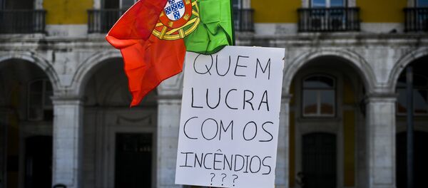 Homem coberto com fita adesiva segura uma bandeira portuguesa e um cartaz dizendo “Quem lucra com os incêndios?”, enquanto centenas de pessoas se juntam na Praça do Comércio, Lisboa, em 21 de outubro de 2017, para protestar contra a resposta do governo aos recentes fogos florestais em Portugal - Sputnik Brasil