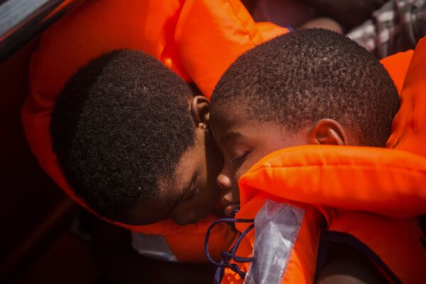 Dois migrantes em barco no Mar Mediterrâneo sendo resgatados. Milhares de refugiados e migrantes tentam chegar à Europa a partir da Líbia e morrem no caminho. - Sputnik Brasil
