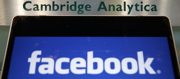 Laptop mostrando logotipo do Facebook é mantido ao lado de uma placa da Cambridge Analytica na entrada do prédio que abriga os escritórios da Cambridge Analytica, no centro de Londres. - Sputnik Brasil
