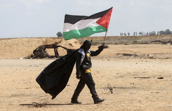Manifestante palestino vestido de Batman segura a bandeira nacional perto da fronteira entre Israel e Faixa de Gaza - Sputnik Brasil
