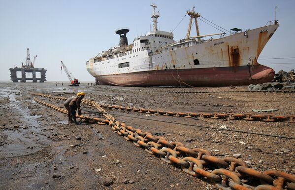 Operários puxam uma corrente ligada a torre de extração de petróleo desmantelada, na Índia - Sputnik Brasil