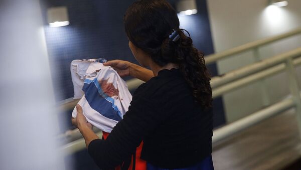 Bruna, mãe do adolescente Marcos Vinicius da Silva, de 14 anos, atingido por uma bala perdida durante operação na favela da Maré, segura camisa da escola que o estudante usava. - Sputnik Brasil