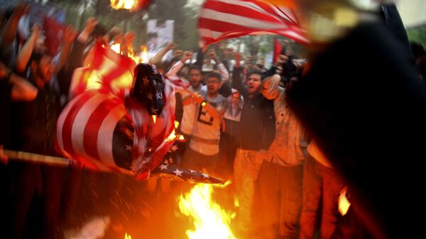 Manifestantes iranianos queimam representações da bandeira dos EUA durante um protesto em frente à ex-embaixada dos Estados Unidos em resposta à decisão do presidente Donald Trump de desistir do acordo nuclear e renovar as sanções a Teerã. - Sputnik Brasil