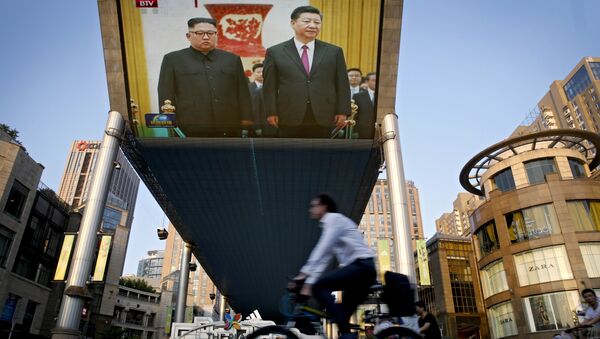As pessoas andam de bicicleta passando por um teção transmitindo a reunião do líder norte-coreano Kim Jong Un e do presidente chinês Xi Jinping durante uma cerimônia de boas-vindas no Grande Salão do Povo em Pequim, terça-feira, 19 de junho de 2018. - Sputnik Brasil