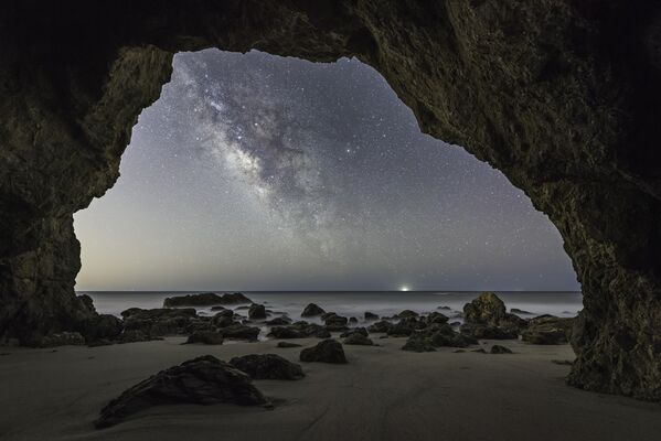 Cave Man por Brandon Yoshizawa. A Via Láctea é vista na abertura de uma caverna marítima. A imagem mostra de perto os detalhes escuros das pedras e luzes distantes da nossa galáxia - Sputnik Brasil