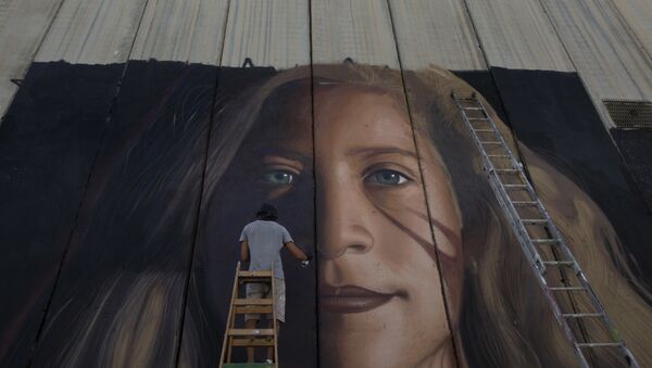 Um artista pinta um mural gigante da ativista palestina Ahed Tamimi em parte da barreira de separação israelense, na Cisjordânia. - Sputnik Brasil