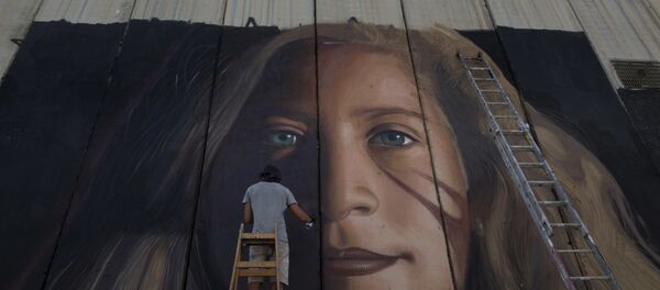 Um artista pinta um mural gigante da ativista palestina Ahed Tamimi em parte da barreira de separação israelense, na Cisjordânia. - Sputnik Brasil
