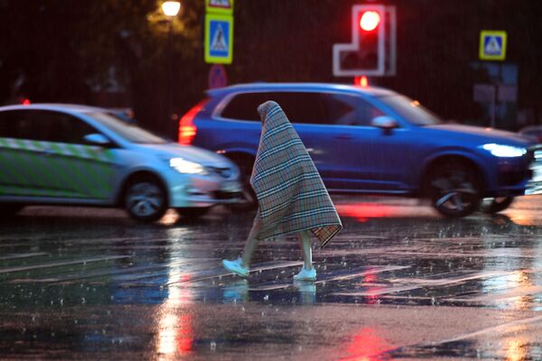 Pedestre passa pela rua durante a chuva, protegido com um cobertor, em Moscou - Sputnik Brasil