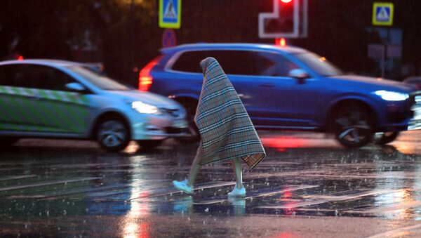 Pedestre passa pela rua durante a chuva, protegido com um cobertor, em Moscou - Sputnik Brasil