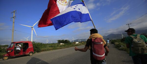 Um migrante carregando as bandeiras do México e de Honduras dá sinal de positivo para um piloto de moto que parou para tirar sua foto, enquanto uma caravana de milhares de pessoas da América Central espera alcançar os limites da fronteira dos EUA a partir de Juchitan, estado de Oaxaca, México. - Sputnik Brasil