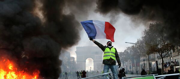Um manifestante segura a bandeira da França sobre uma barricada em chamas na Avendia Champs-Elysees, com o arco do Triunfo ao fundo, durante a manifestação contra o aumento de combustíveis no país. Foto de 24 de novembro de 2018. - Sputnik Brasil