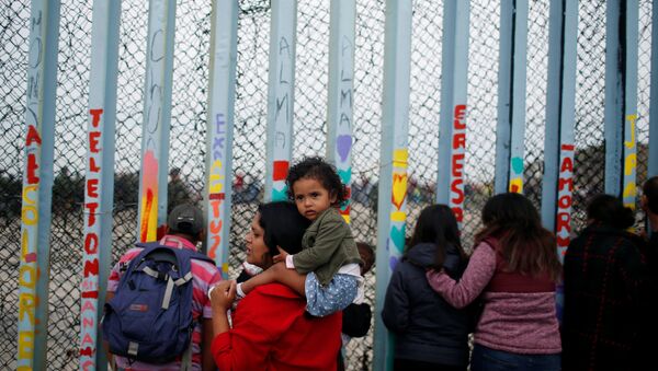 Uma mulher é fotografada com o filho reunião em apoio à caravana de migrantes em San Diego, EUA, perto da fronteira entre os Estados Unidos e o México, em Tijuana. - Sputnik Brasil