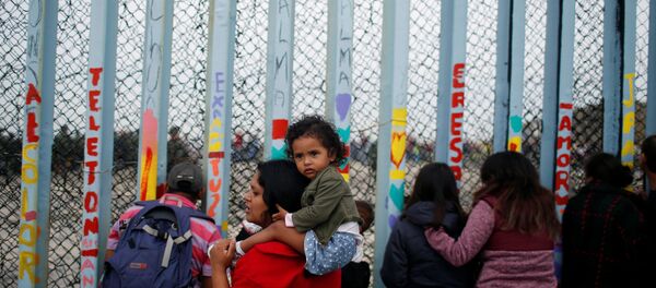 Uma mulher é fotografada com o filho reunião em apoio à caravana de migrantes em San Diego, EUA, perto da fronteira entre os Estados Unidos e o México, em Tijuana. - Sputnik Brasil