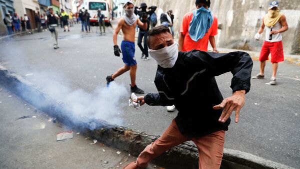 Manifestante joga bomba de gás lacrimogêneo de volta contra Guarda Nacional venezuelana durante protesto em Caracas, Venezuela, em 21 de janeiro de 2019 - Sputnik Brasil