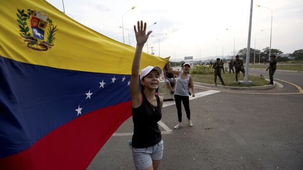 Mulher grita bem-vinda ajuda humanitária, balançando bandeira venezuelana em frente a grupo de soldados do Exército venezuelano e oficiais da Guarda Nacional bloqueando o acesso principal à ponte internacional Tienditas, que liga Colômbia e Venezuela, 7 de fevereiro de 2019 - Sputnik Brasil