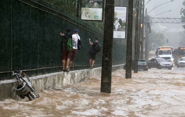 Moradores se seguram em grade para atravessar rua alagada no Rio de Janeiro - Sputnik Brasil