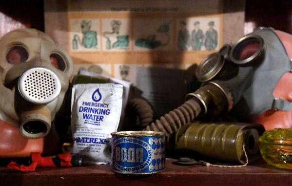 Ao fundo, cartaz de instruções, com lata e saquinho de água da época soviética, que deveria ser tomada em caso de carência de recurso, rodeados de máscaras - Sputnik Brasil